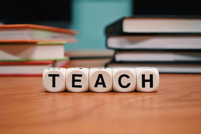 nápis „uč“ nebo „učit“ poskládaný z kostek před knihami na stole